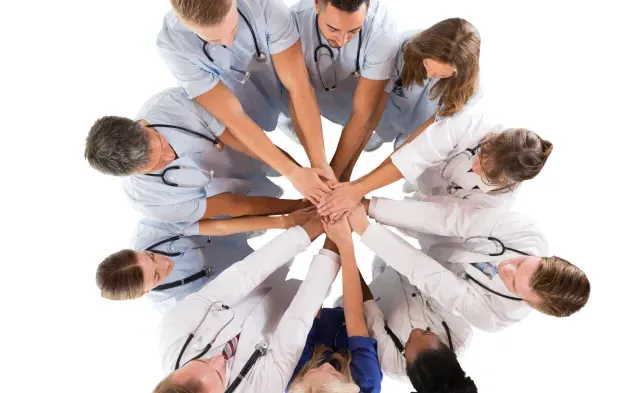 Group of medical professionals in a huddle with their hands stacked in the middle