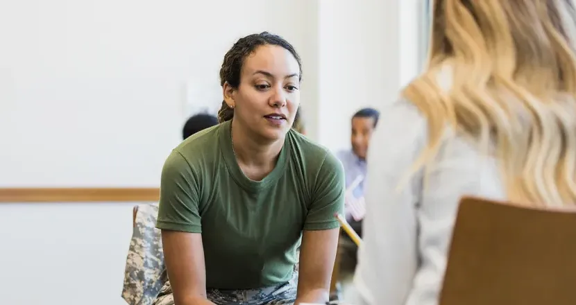 Military service member in uniform having a focused conversation with a counselor or advisor, discussing support and opportunities.